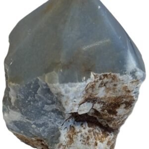 Natural rough angelite freeform crystal with unpolished sides and a smooth polished blue point standing on a white background
